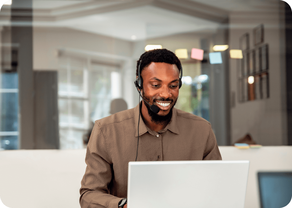 Man smiling while using laptop and headset.